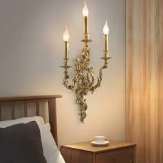 Ornate gold wall sconce with three candle-style lights in a luxury bedroom setting, adding elegance and ambient lighting. Perfect for upscale home décor and interior design inspiration.