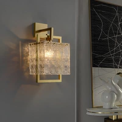 Elegant modern wall sconce with a textured glass shade and gold geometric details, ideal for upscale interior decor and lighting.