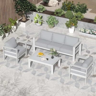Bright modern outdoor patio furniture set with white sofas and armchairs, complemented by potted plants and greenery, perfect for stylish outdoor relaxation.