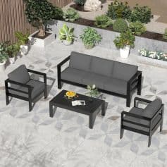 Modern outdoor garden furniture set with black frames and gray cushions, including a sofa and armchairs, situated in a stylish patio surrounded by potted plants and decorative greenery for a relaxing atmosphere.