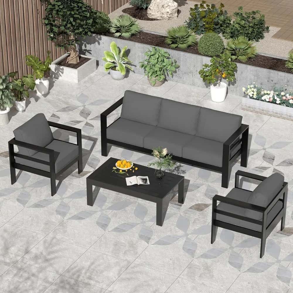 Modern outdoor garden furniture set with black frames and gray cushions, including a sofa and armchairs, situated in a stylish patio surrounded by potted plants and decorative greenery for a relaxing atmosphere.