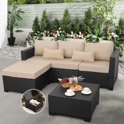 Natural outdoor sectional sofa with beige cushions on black wicker frame, surrounded by lush greenery and flowering plants, perfect for patio relaxation and outdoor living.
