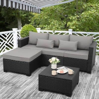 Outdoor patio furniture set with dark wicker design, cushions, and a small table with coffee mugs, flowers, and magazines, perfect for relaxing or entertaining in a garden or backyard setting.