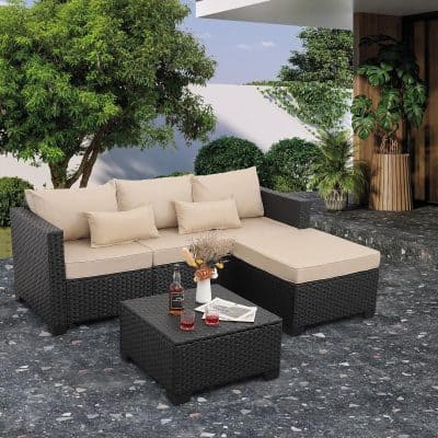 Elegant outdoor wicker sofa set with beige cushions and matching ottoman on a stylish patio, surrounded by lush greenery and modern decor, perfect for relaxing or entertaining.
