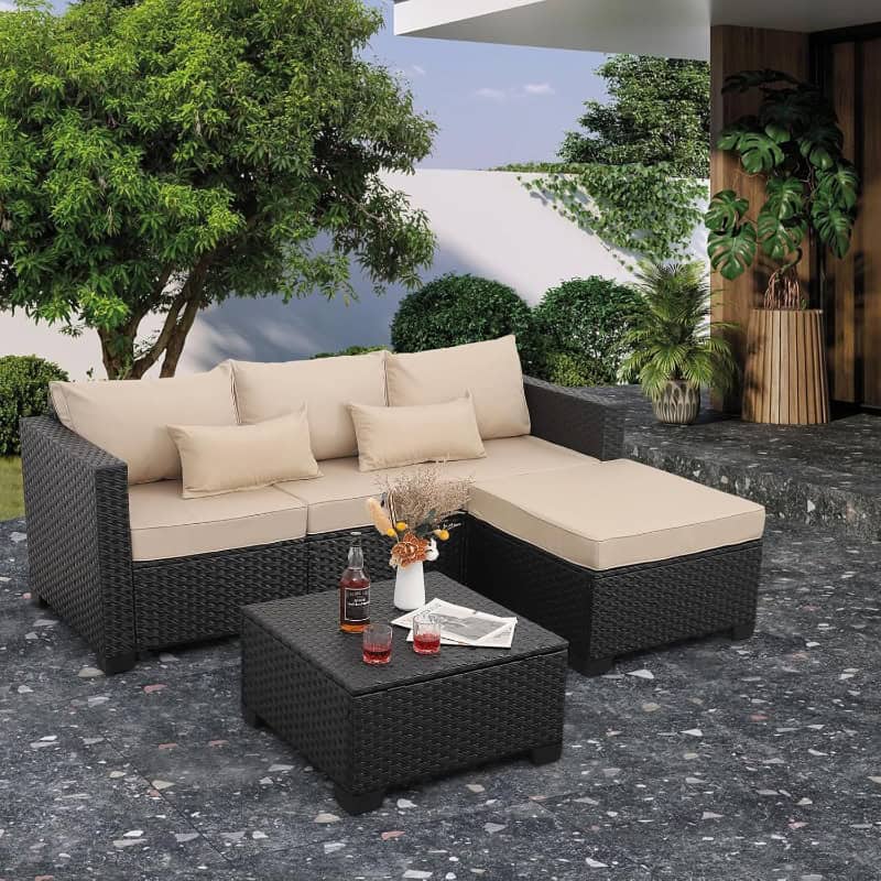 Elegant outdoor wicker sofa set with beige cushions and matching ottoman on a stylish patio, surrounded by lush greenery and modern decor, perfect for relaxing or entertaining.