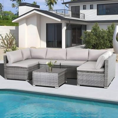 Modern outdoor lounge area with stylish sectional sofa, glass-topped coffee table, pool, and contemporary house, perfect for relaxing and entertaining in a luxurious residence.