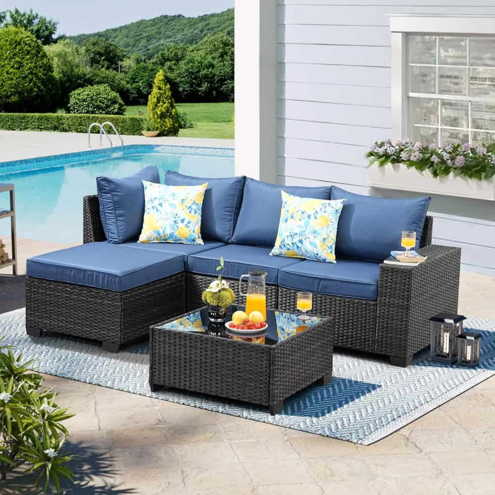 Luxury outdoor patio furniture set with navy cushions and floral pillows, perfect for relaxing by the poolside on a sunny day.