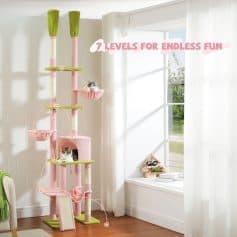 Pink and green multi-level cat tree with cozy perches, hideouts, and scratching posts in a bright room with white walls and large window, perfect for entertainment and exercise.