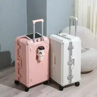 Pink and white hard-shell suitcases with telescopic handles, one with a disposable coffee cup attached, placed on wooden floor near a cozy chair and a wall, ideal for travel and luggage storage at Monalisa Store.