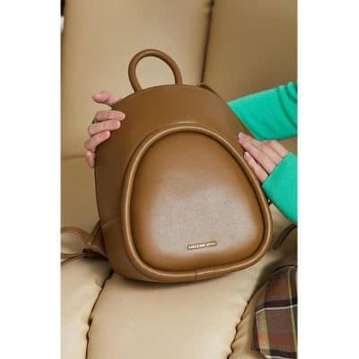 Backpack with "Amazing Song" logo resting on beige couch, held by person in teal sweater, highlighting stylish and functional design for everyday use.