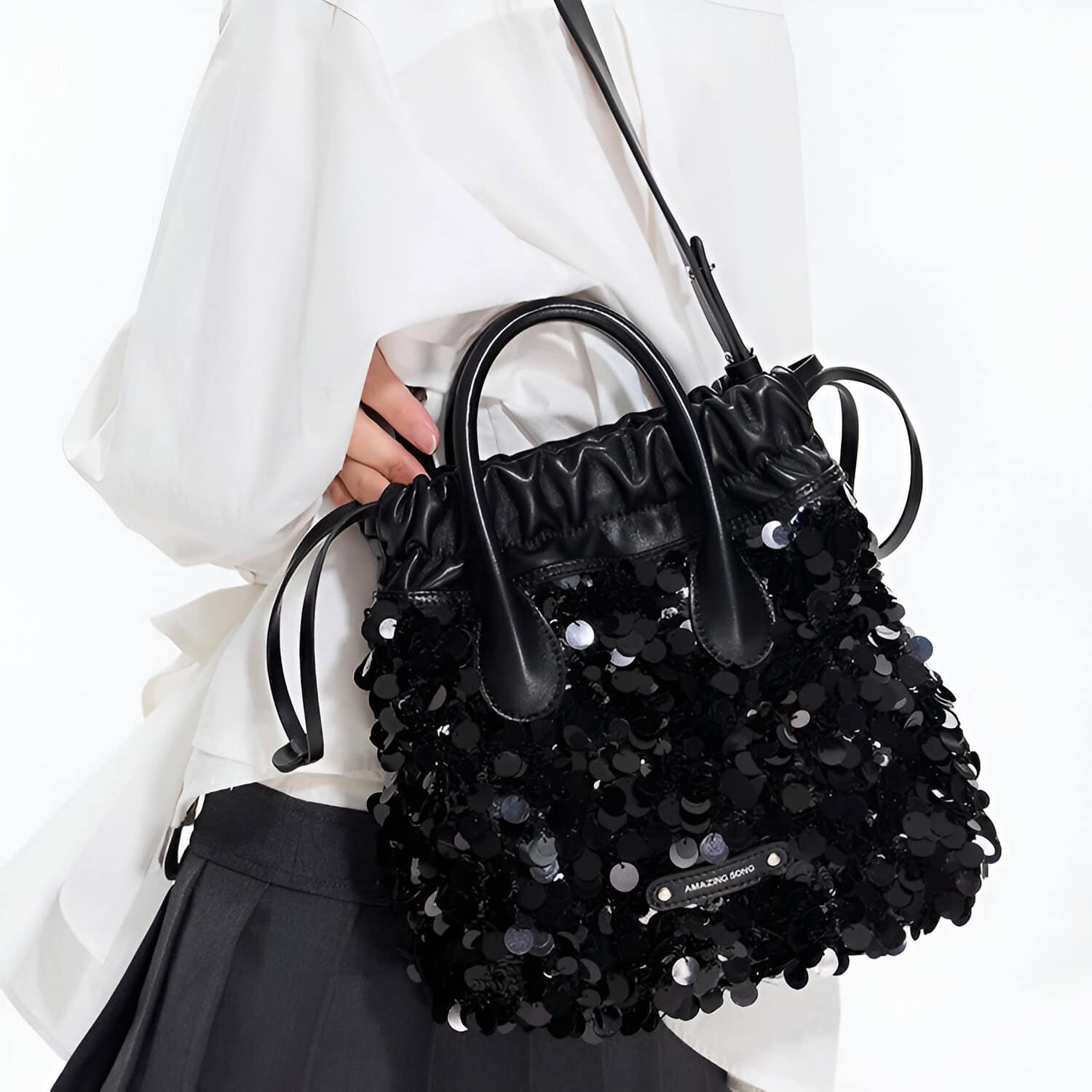 Shiny black sequined handbag with leather accents, held by a person wearing a white blouse and dark trousers at Monalisa Medical Store.