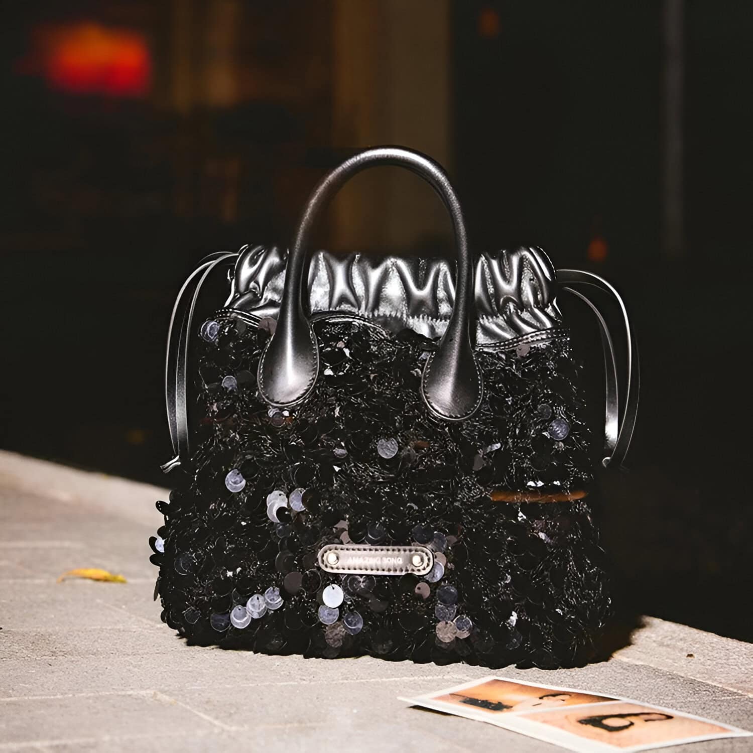 Black sequined fashion handbag with metallic handles and luxury branding, ideal for stylish accessories and high-end fashion statements.