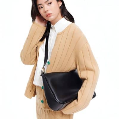 Elegant woman in beige cardigan and white shirt holding black leather handbag, showcasing women's fashion accessories, trend-setting style, and fashionable handbag collection from Monalisa Store.