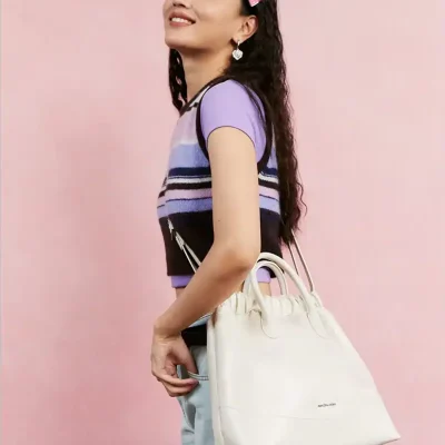 Elegant woman carrying a stylish white handbag, featuring the Monalisa Store logo, with a pink background and casual trendy outfit, showcasing luxury accessories for optical fashion.