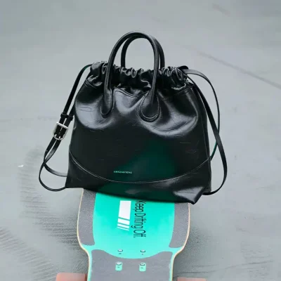 Stylish black leather handbag placed on a skateboard with a turquoise grip tape at Monalisa Medical Store, showcasing fashionable accessories and essential items for modern lifestyles.