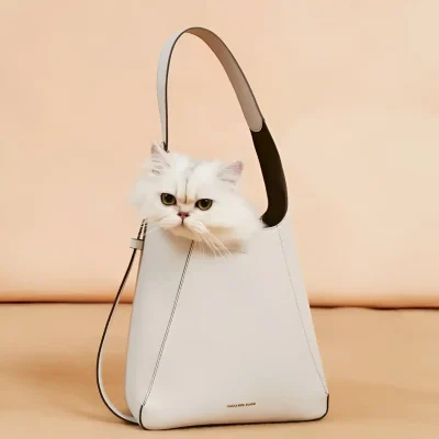 Fluffy white Persian cat with yellow eyes peeking out of a sleek, modern white handbag on a peach background, showcasing luxury pet accessories from Monalisa Store.