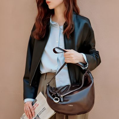 High-quality image of a stylish woman holding a brown leather handbag and a newspaper, dressed in a professional outfit with a leather jacket and light blue shirt, at Monalisa Store specializing in optical solutions.