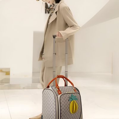 Gucci patterned rolling suitcase with a fun pineapple and teal leaf keychain, perfect for travel; stylish and practical design from Monalisa Store.