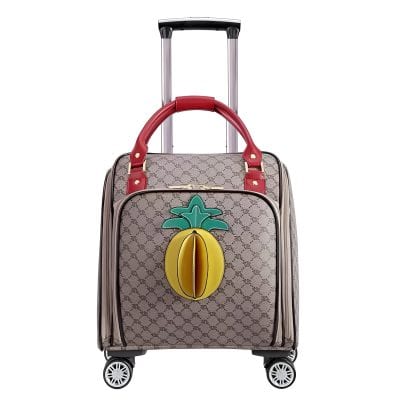 Vibrant designer tote with pineapple applique on patterned travel luggage trolley for stylish airport travel.