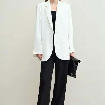 Elegant woman in a white blazer and black pants, showcasing professional office fashion, wearing glasses, holding a black clutch, representing stylish workplace attire for women.