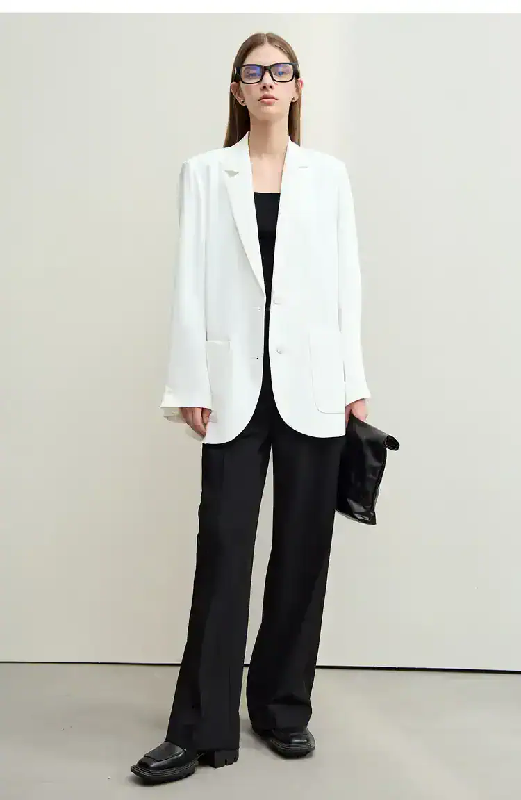 Elegant woman in a white blazer and black pants, showcasing professional office fashion, wearing glasses, holding a black clutch, representing stylish workplace attire for women.