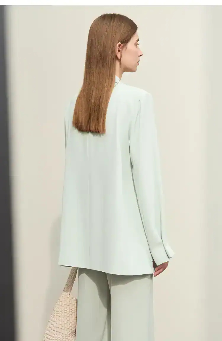 Elegant woman with straight auburn hair wearing a white blazer and wide-leg trousers, holding a textured handbag, showcasing sophisticated fashion and style for Monalisa Medical Store.