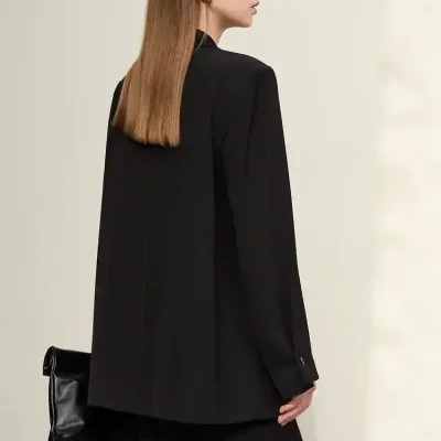 Elegant woman in black blazer and skirt with a stylish bag, showcasing modern fashion accessories at Monalisa Store for sophisticated eyewear and optical solutions.