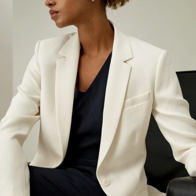 Professional woman in elegant white blazer and black top, seated in an office setting, showcasing stylish professional attire, ideal for vision care and eye health services at Monalisa Store.