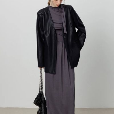 Stylish woman in black leather blazer, gray dress, sneakers, holding a black chain-strap bag, standing against a plain white background at Monalisa Store.