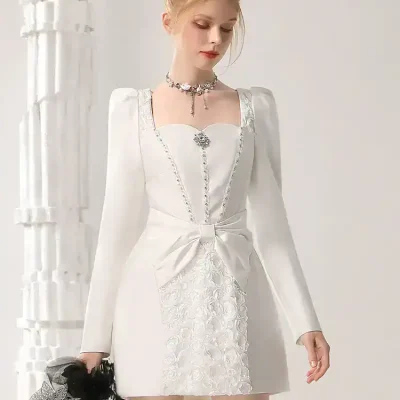 Elegant white formal dress with intricate embroidery and bow detail, perfect for special occasions, stylish wedding guest attire, or upscale events. Features long sleeves, a fitted silhouette, and decorative accessories.