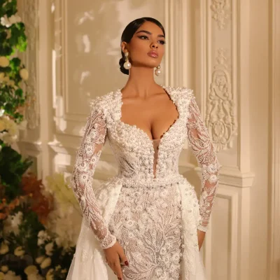 Elegant bridal gown featuring intricate pearl and lace embellishments, long lace sleeves, plunging neckline, and sophisticated floral embroidery, perfect for wedding or special occasions.