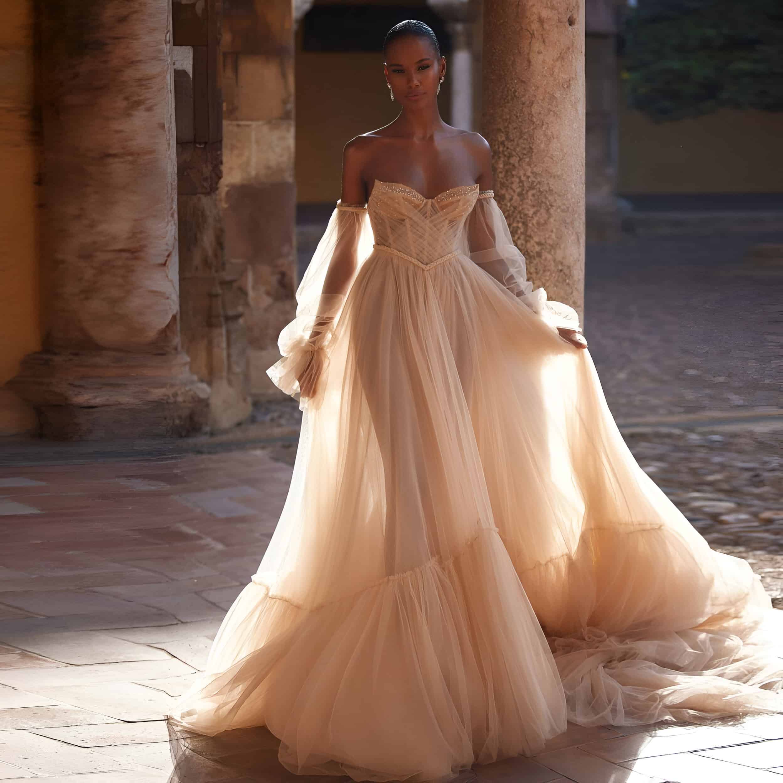 Elegant peach-colored off-shoulder gown with sheer draped sleeves, ideal for bridal or special occasionwear at Monalisa Store.