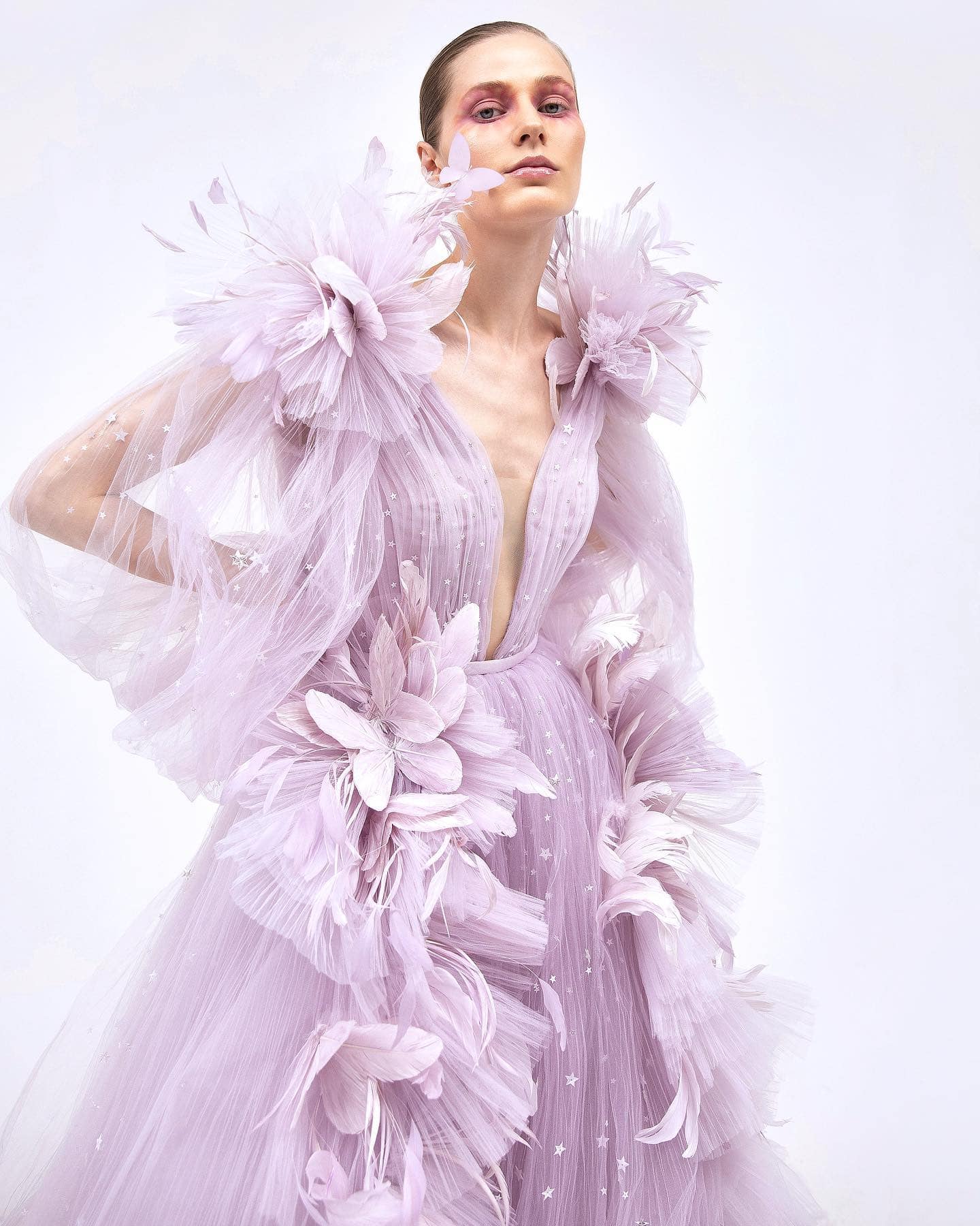 Elegant fashion model wearing a pastel pink tulle dress with floral and butterfly embellishments, showcasing Monalisa Store's high-end designer clothing collection and accessories for modern, stylish women.