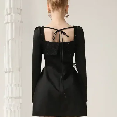 Elegant black dress with unique back detailing, perfect for fashionable occasions or stylish events. Features long sleeves, subtle shimmer, and a flattering silhouette for a sophisticated look.