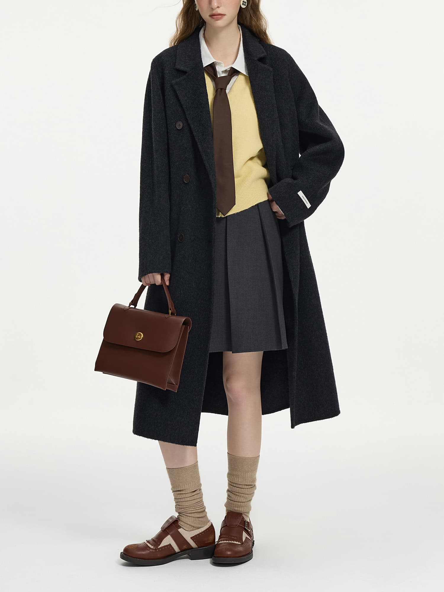 Stylish woman in fall fashion with oversized black coat, grey pleated skirt, mustard sweater, brown accessories, and leather shoes, showcasing trendy fall and winter wardrobe essentials at Monalisa Store.