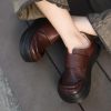 Brown leather chunky platform shoes with black soles, worn by a person sitting on a grey tiled floor, showcasing trendy footwear fashion at Monalisa Store.