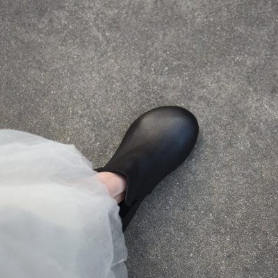 Black leather slip-on shoe on gray textured pavement, fashion-forward footwear focus.