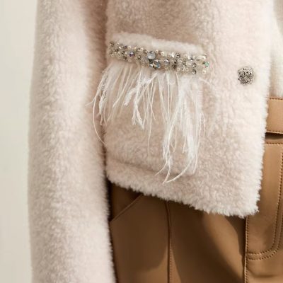 Luxurious beige teddy coat with pearl and rhinestone embellishments, feather details, and elegant buttons, perfect for fashionable winter wear.
