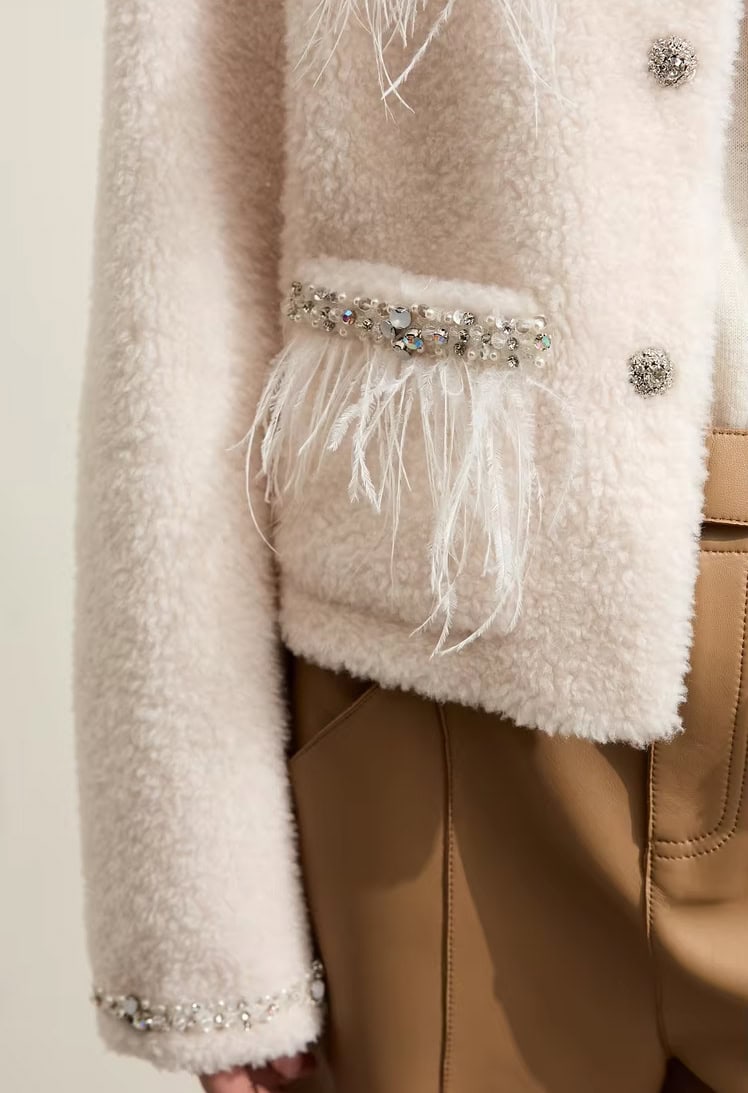 Luxurious beige teddy coat with pearl and rhinestone embellishments, feather details, and elegant buttons, perfect for fashionable winter wear.