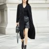 Black stylish women's trench coat and leather shorts perfect for fall fashion. Sophisticated city look with ankle boots and handbag, ideal for professional or casual outings.