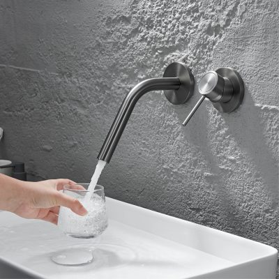 Modern stainless steel wall-mounted faucet in a contemporary kitchen or bathroom setting, with a hand filling a glass with water. Focus on sleek design, durable material, and functional hygiene features for home or commercial use.