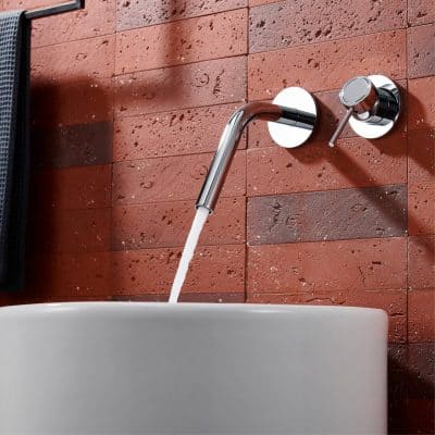 Shower faucet with a modern chrome finish mounted on a red brick wall in a bathroom setting.