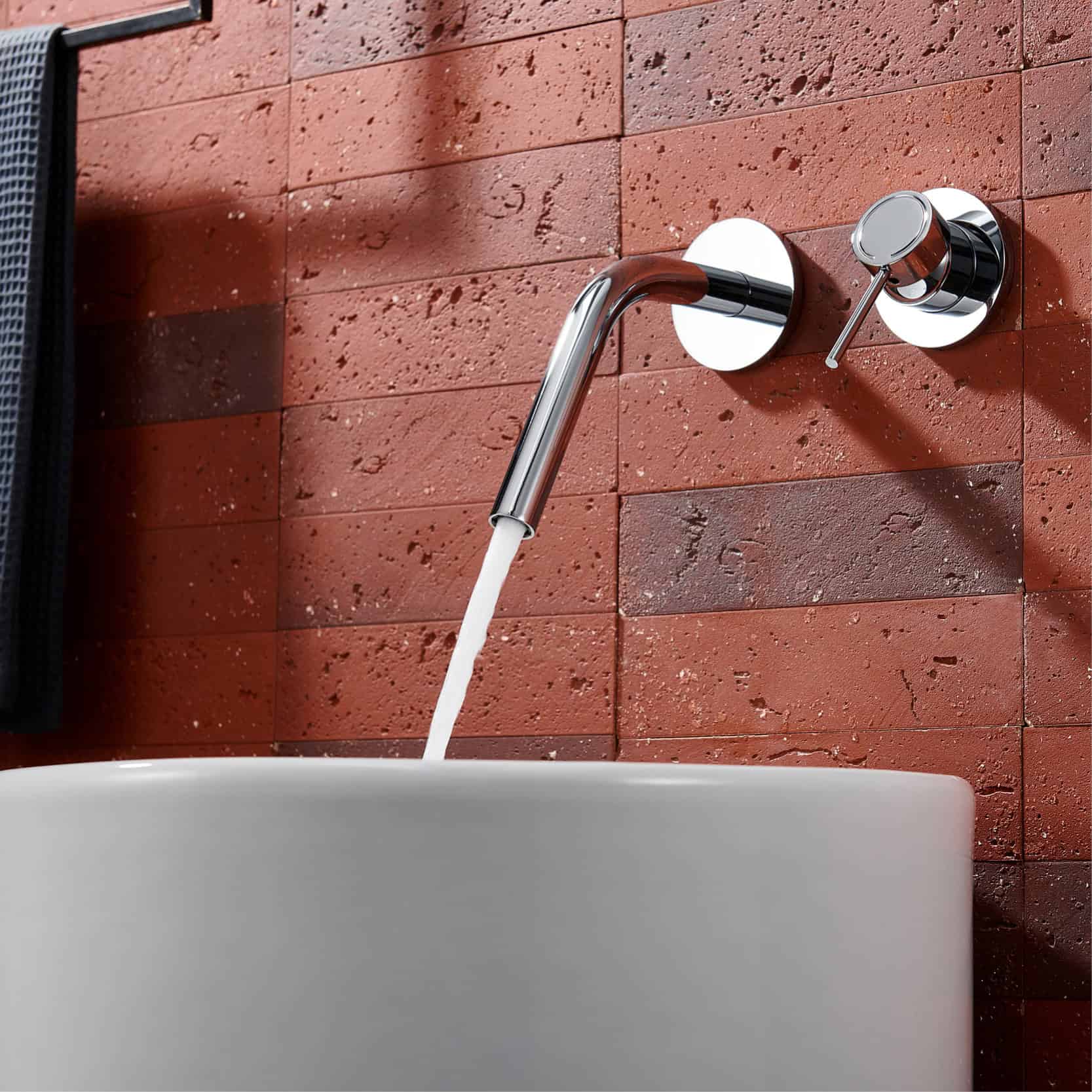 Shower faucet with a modern chrome finish mounted on a red brick wall in a bathroom setting.