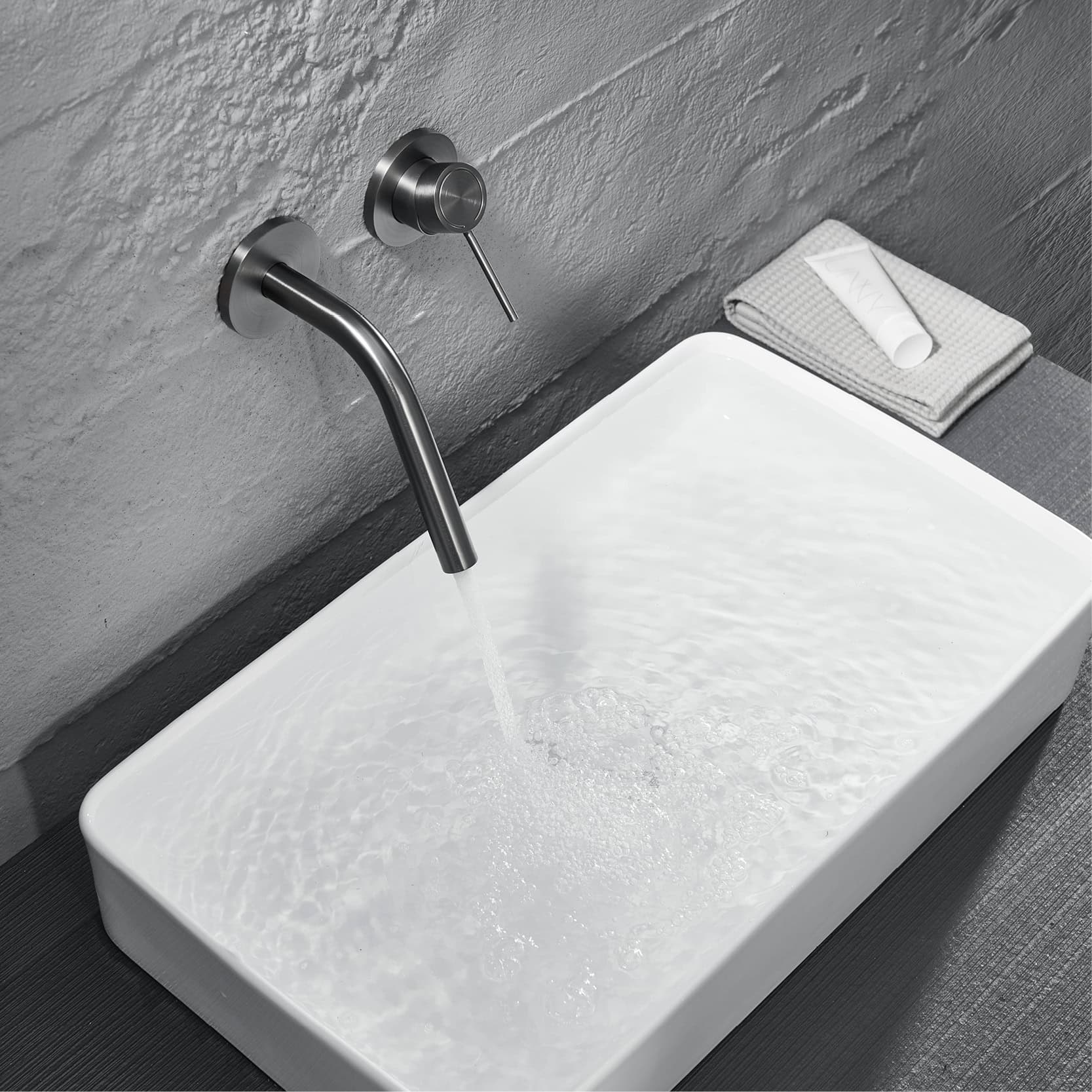 Sleek modern black wall-mounted faucet above a stylish white rectangular vessel sink with gentle water flow. Neatly folded towel and skincare product placed nearby in contemporary bathroom setting.