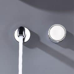 Shiny faucet with running water and a nearby round light source on a gray wall, modern bathroom fixture.