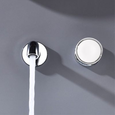 Shiny faucet with running water and a nearby round light source on a gray wall, modern bathroom fixture.