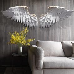 Elegant white angel wing wall art decor over a modern beige sofa with a side table holding yellow flowers, creating a serene and stylish ambiance in the Monalisa Medical Store interior.