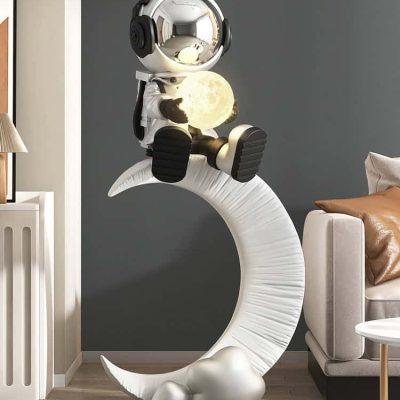 Moon lamp with astronaut figurine sitting on a crescent moon sculpture in modern living room decor.