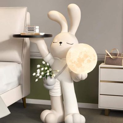 Cute rabbit-shaped lamp holding a moon-shaped light with a small flower bouquet, modern bedroom decor, Monalisa Store, stylish nightlight, whimsical home accessory, cozy lighting, adorable figurine, contemporary interior decor, animal-shaped lamp.