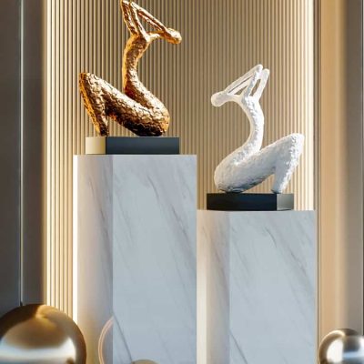 Elegant swan sculptures displayed on marble pedestal stands, featuring gold and white finishes, surrounded by decorative metallic spheres, showcasing luxurious decor at Monalisa Store for modern interiors.